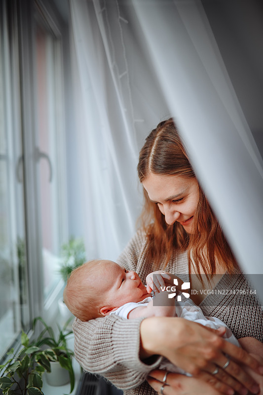 温柔的母亲在窗边摇晃，怀中抱着婴儿。图片素材