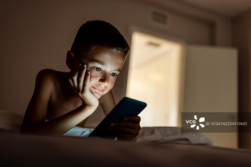 男孩在晚上躺在床上玩手机图片素材