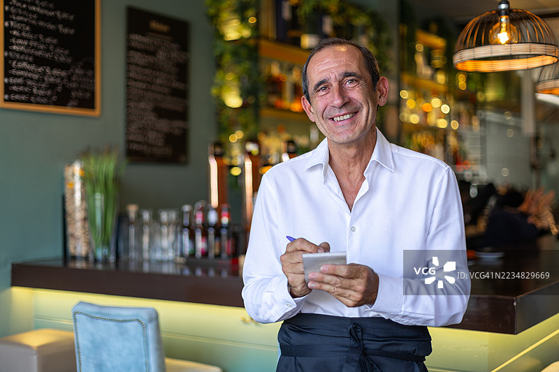 微笑着对着镜头的资深服务员在餐厅中点餐图片素材