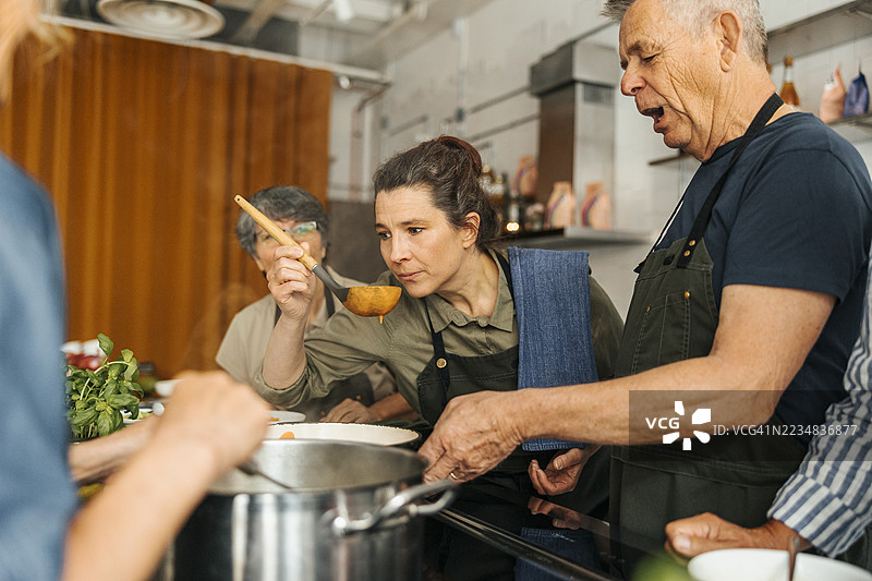 女性厨师在商业厨房的烹饪课堂上闻着由一位年长男性制作的酱汁图片素材
