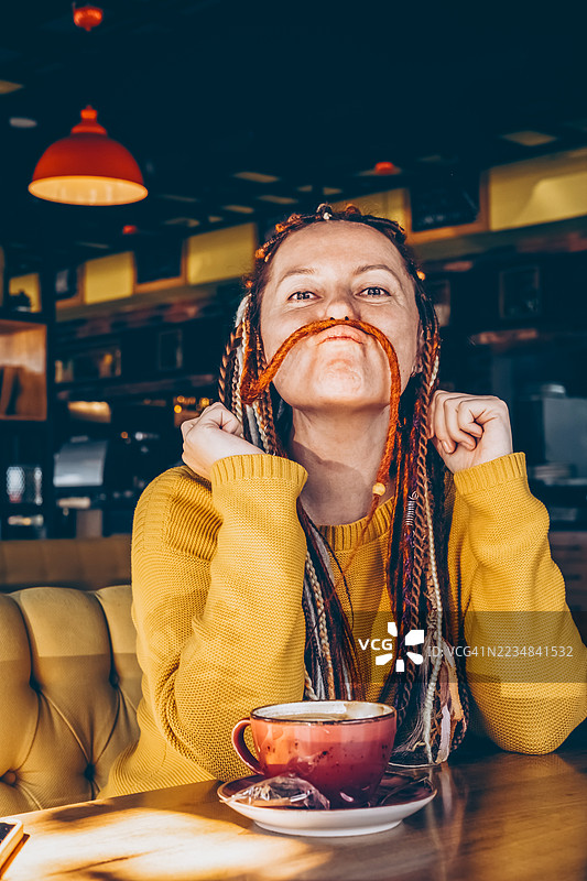 咖啡馆里的女人把辫子当作胡子。顽皮的表情和有趣的时刻概念。图片素材