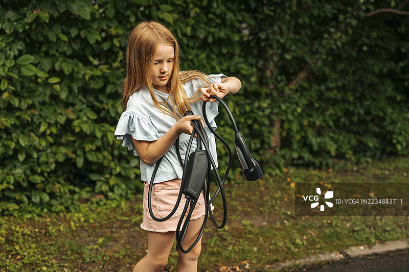 金发女孩手持电插头，站在植物旁边图片素材