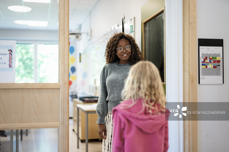 微笑的女老师在教室门口迎接站着的女孩图片素材