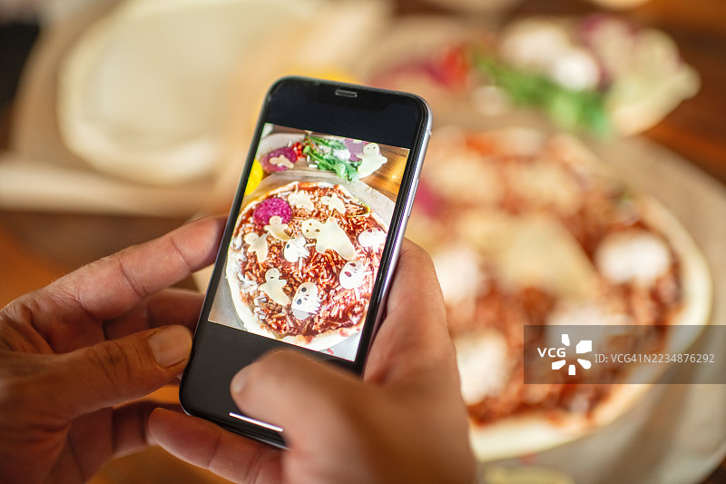 男子用智能手机拍摄万圣节披萨的照片图片素材