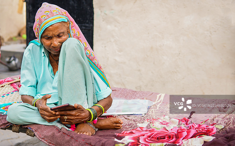传统的印度农村老年女性坐在查尔派上使用智能手机。图片素材