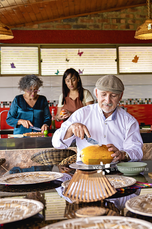 祖父在厨房里剥水果，家人们一起做饭。图片素材