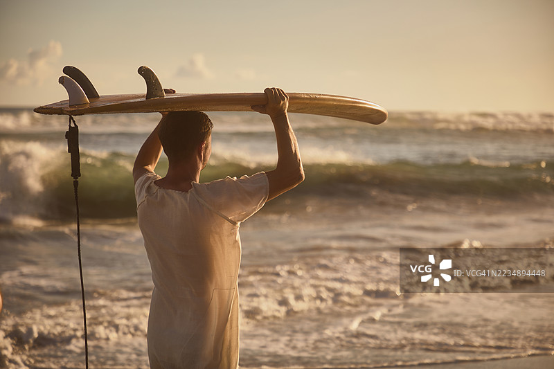 冲浪者在海边手持冲浪板，背景是波涛汹涌的海浪图片素材
