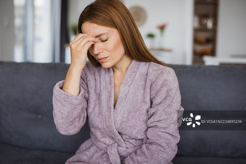 女人坐在家里的沙发上，饱受剧烈头痛的折磨。图片素材