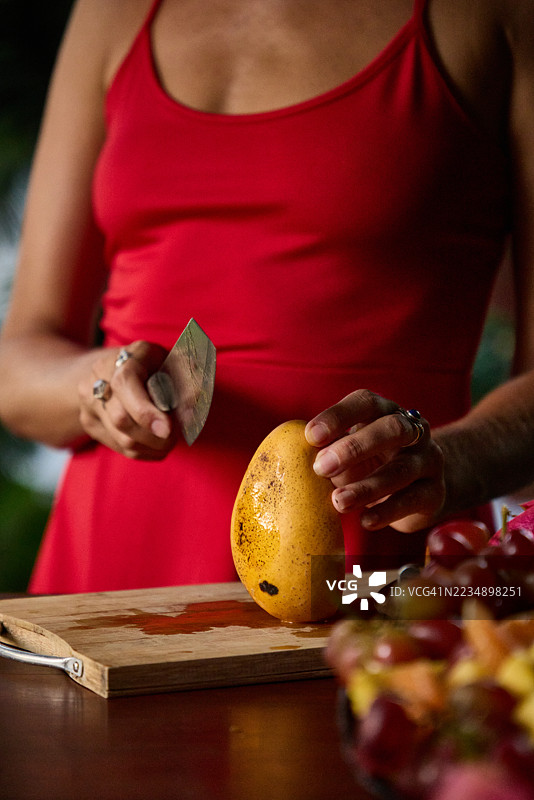 在木砧板上剥芒果的人，周围环绕着色彩鲜艳的水果图片素材