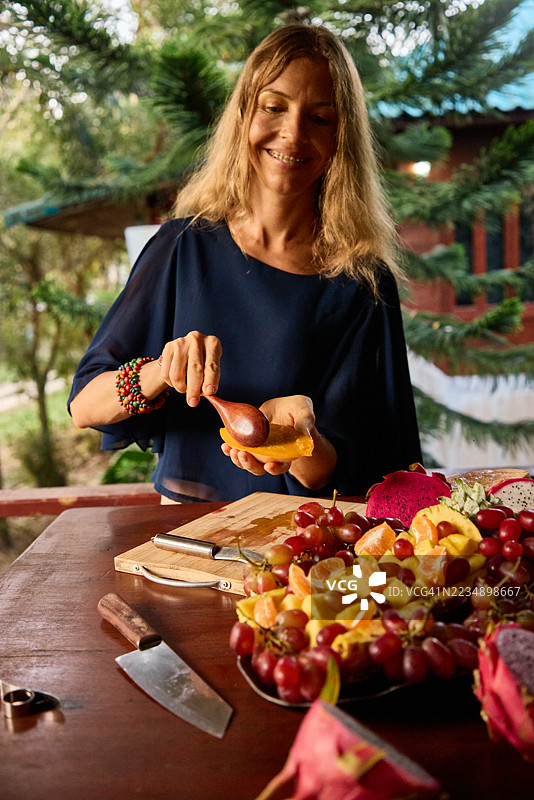 一位女士在乡村户外木桌上准备新鲜水果，面带微笑图片素材