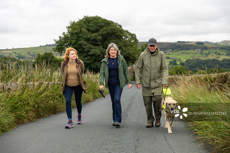 一家三口与导盲犬在乡村小路上散步图片素材