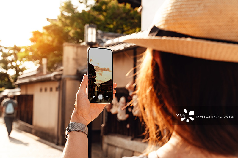 从肩后角度看，年轻女子在日本京都古镇用智能手机拍照图片素材
