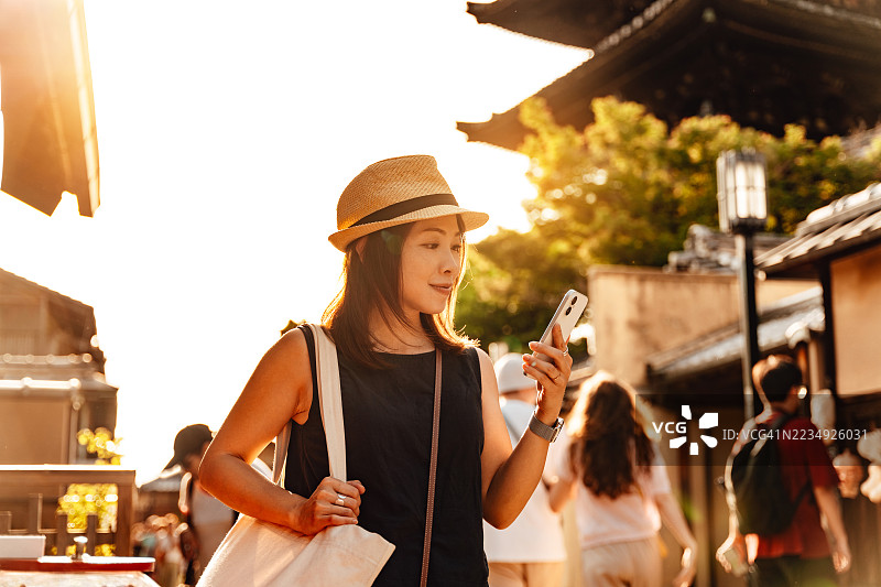 日本京都古城里，一位女性游客正拿着智能手机行走。图片素材