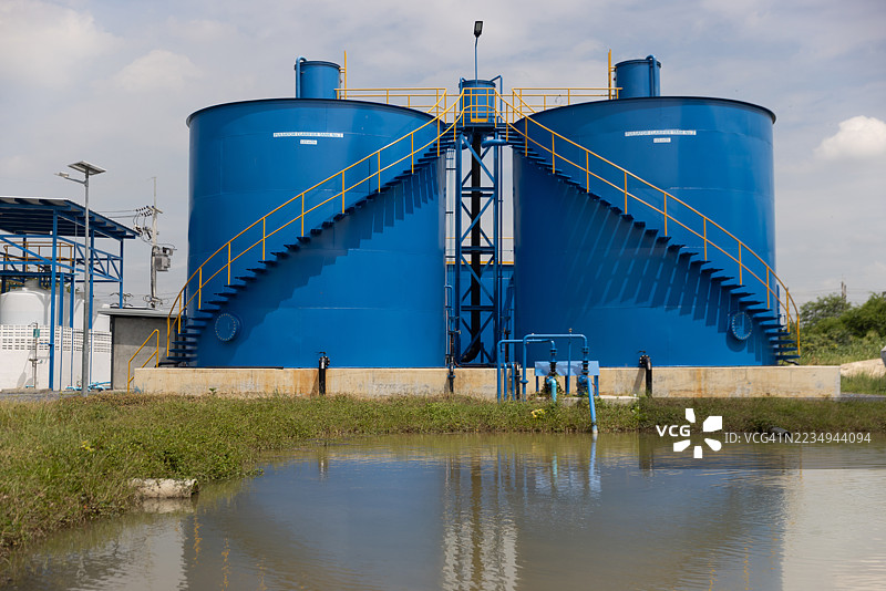 两名环境科学家穿着防护工作服和发网，携带水质检测的硬壳设备，在水处理设施现场工作。图片素材