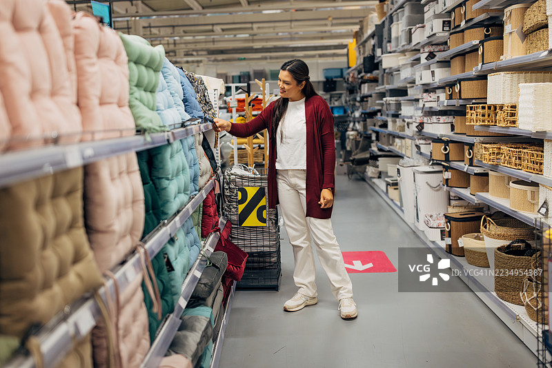 女人在为阳台或露台椅子挑选靠垫。她正在检查垫子的面料和舒适度，周围是其他户外家居配件。图片素材