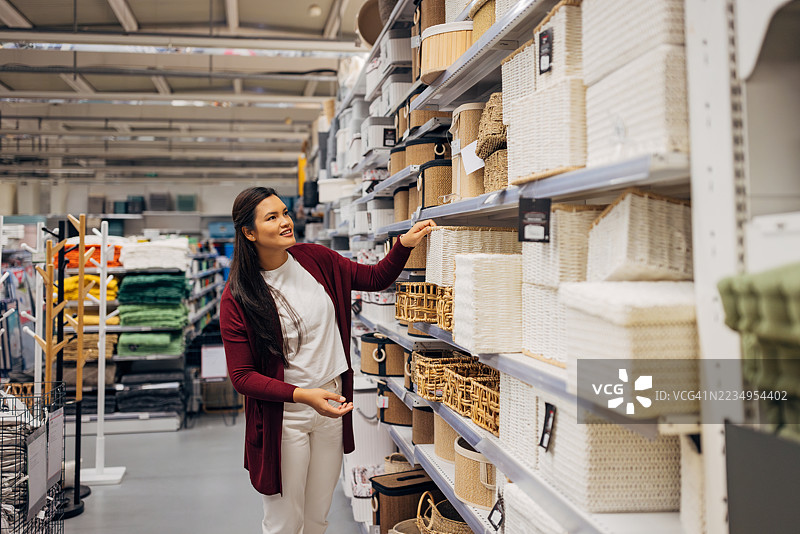 亚洲女性在查看满是储物和整理产品的货架。商店展示了各种质地和尺寸的产品，包括天然编织的篮子。图片素材