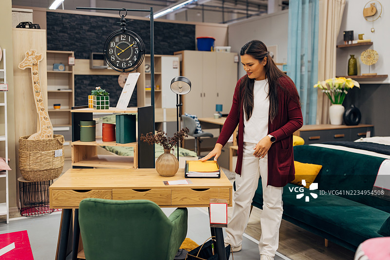 一位女性顾客正在家具店研究购买桌子的不同选择。图片素材