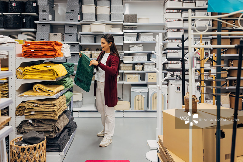 女性顾客在家居用品店浏览浴室地垫。她正在查看各种柔软的垫子，按颜色和尺寸排列，适合放在马桶或淋浴间前使用。图片素材