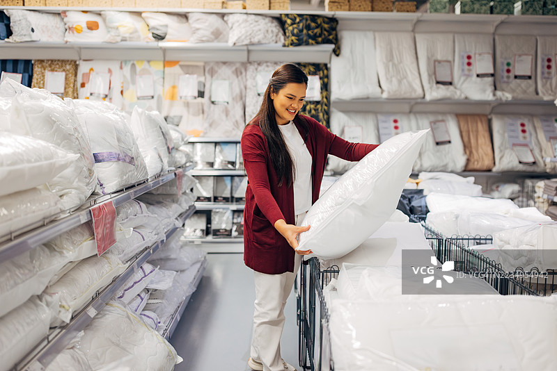 微笑的亚洲女性在现代家居店挑选卧室枕头图片素材