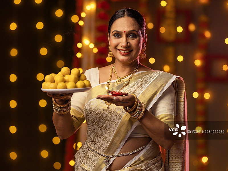 在排灯节期间，家中快乐的女人手持油灯和甜点。图片素材