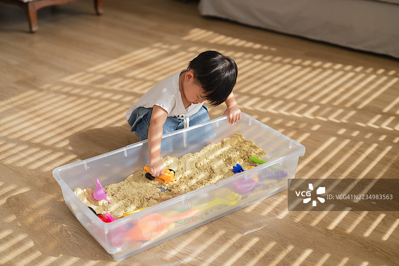 顽皮快乐的幼儿与父母一起享受愉快的周末，在家中玩防水沙。小男孩在家里的沙箱中进行感官游戏，帮助锻炼手指肌肉。图片素材