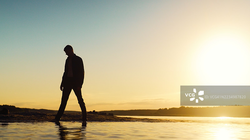 日落时分，一个迷失的男人在浅水中行走的剪影。寻找生活的意义。图片素材