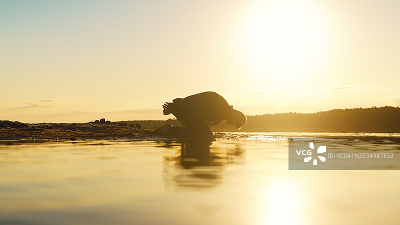 日落时分，浅水中跪着的男人剪影，陷入绝望。图片素材
