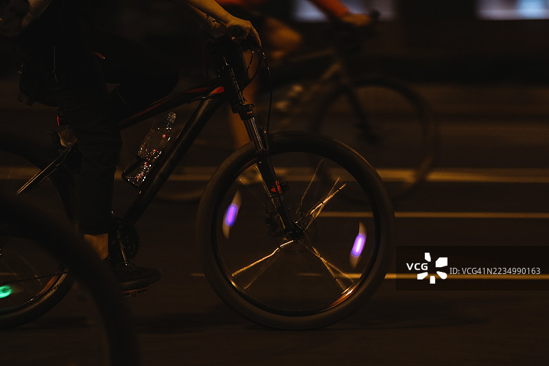 夜晚城市生活，低角度骑自行车者快速骑行，霓虹色轮子在夜晚闪耀图片素材