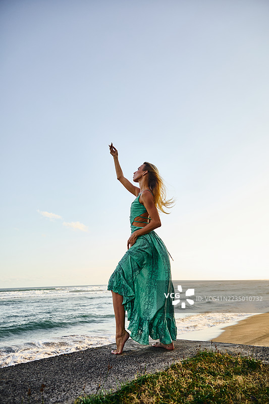 穿着绿色裙子的女人在日落时分的海滩上跳舞图片素材