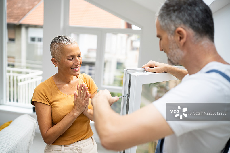 一位男士正在维修家中窗户，一位女士在一旁鼓掌赞赏图片素材