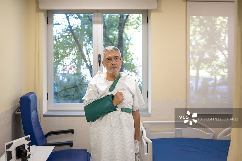 穿着医院病服和吊带的男性病人坐在床边，面向镜头。图片素材