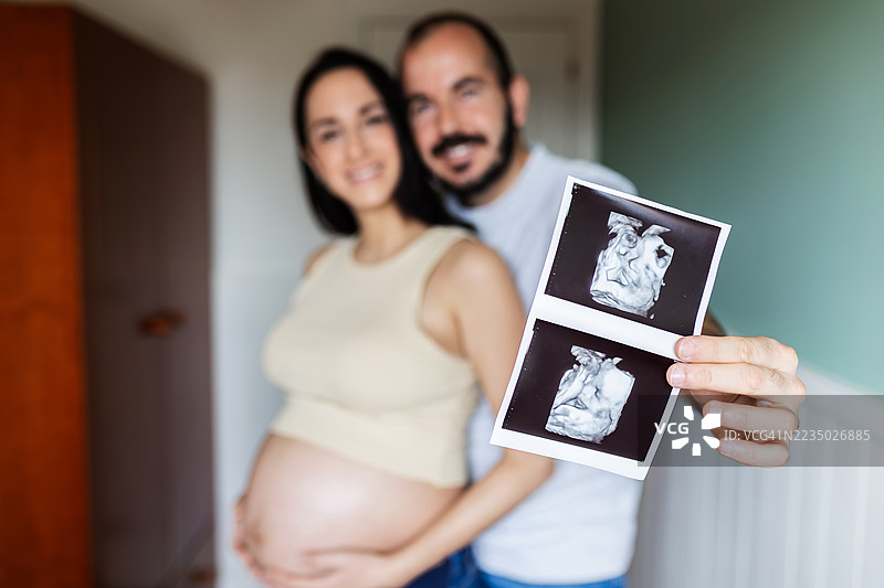 快乐的孕妇夫妇展示宝宝的超声波扫描图图片素材
