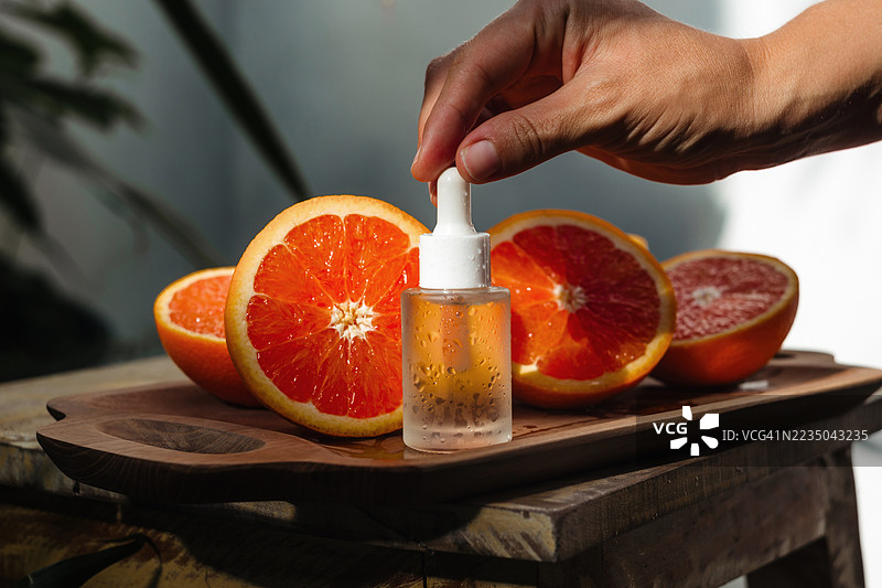 女人的手在橙子旁边打开面部精华，准备使用天然维生素C精华的特写镜头。图片素材