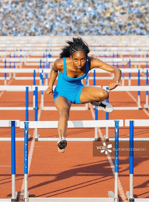 身穿蓝色运动服的运动员在户外跑道上跳过障碍，参加比赛。美国图片素材
