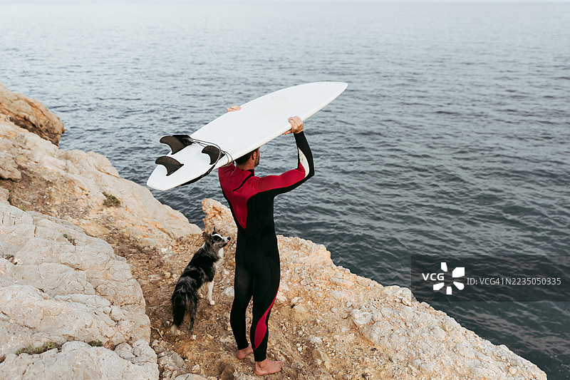 冲浪者手持冲浪板，和他的狗一起望向海洋图片素材