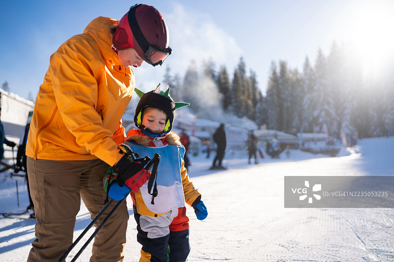母亲在阳光明媚的冬季风景中指导孩子滑雪图片素材