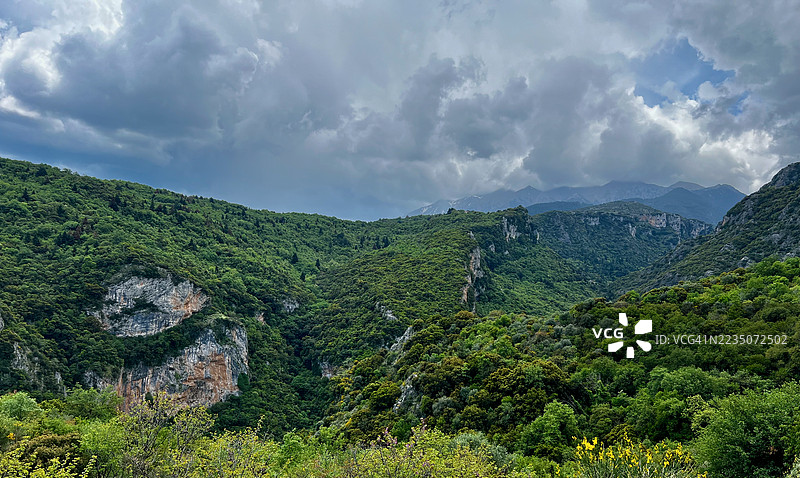 希腊郁郁葱葱的绿色山脉和山谷在戏剧性的多云天空下，展现出充满活力的自然风光。图片素材