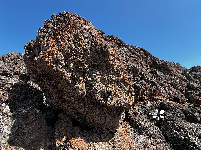 希腊清澈蓝天下的崎岖火山岩石地貌图片素材