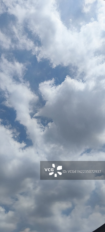 低角度视图下，广阔的蓝天中布满了戏剧性的蓬松白云和灰云，营造出宁静而广袤的自然背景。图片素材