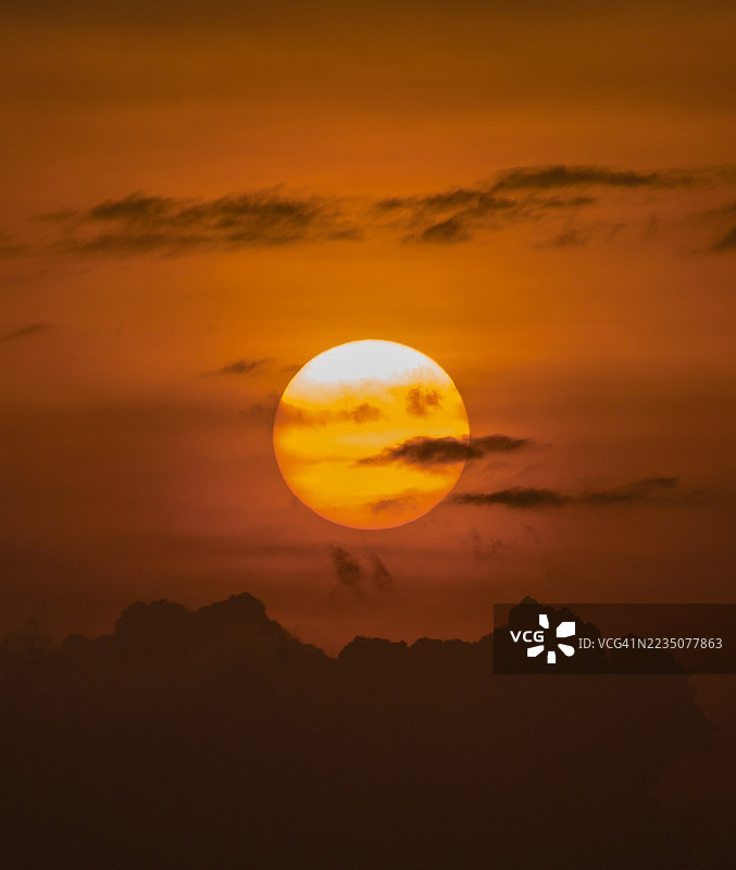 戏剧性的日落，巨大的太阳圆盘在剪影般的山脉和云朵上方图片素材