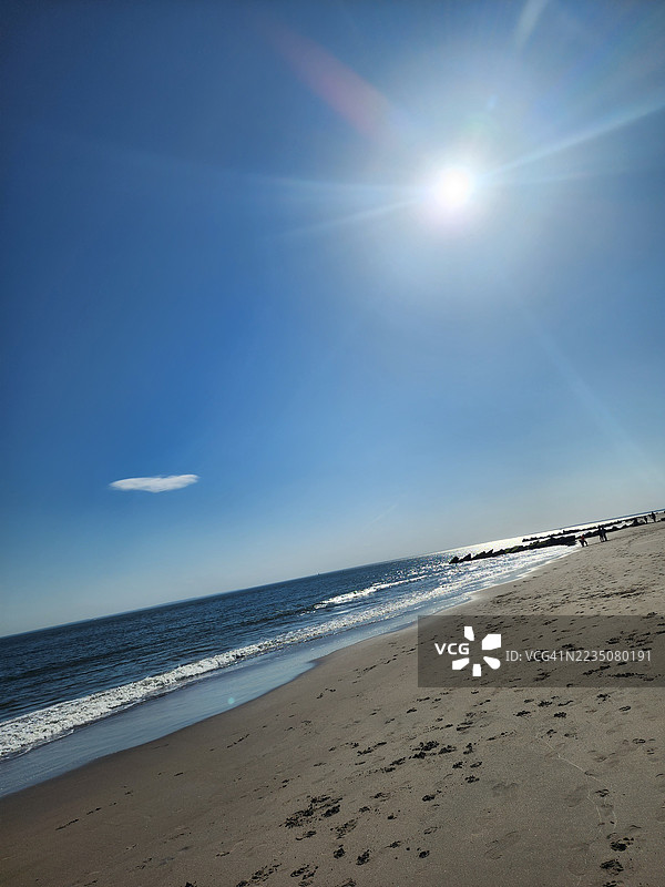 明亮的阳光照耀着平静的海滩，轻柔的海浪和湛蓝的天空相映成趣。图片素材