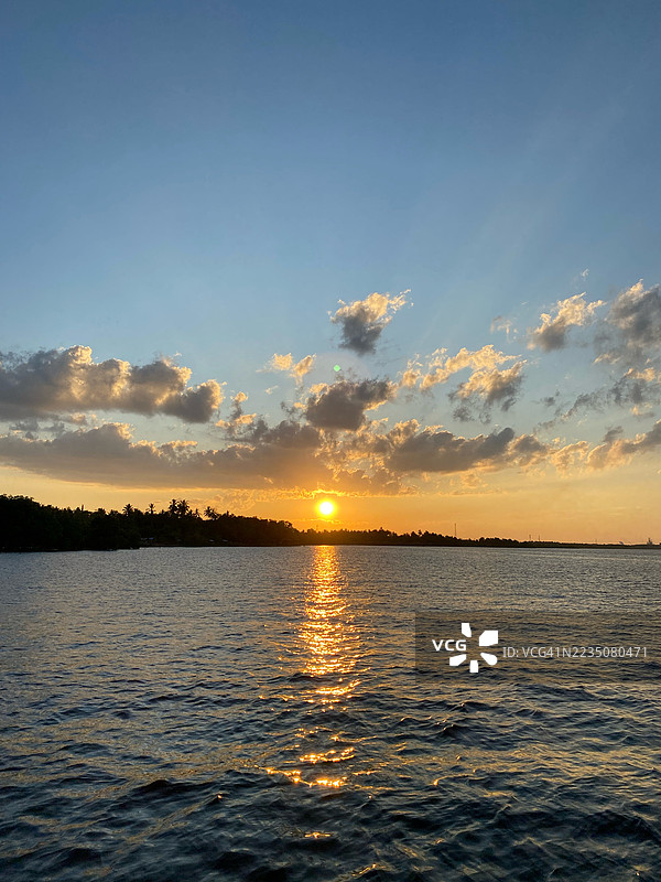 金色日落映照在宁静的海面上，远处的海岸线在水面上反射出温暖的光线。图片素材