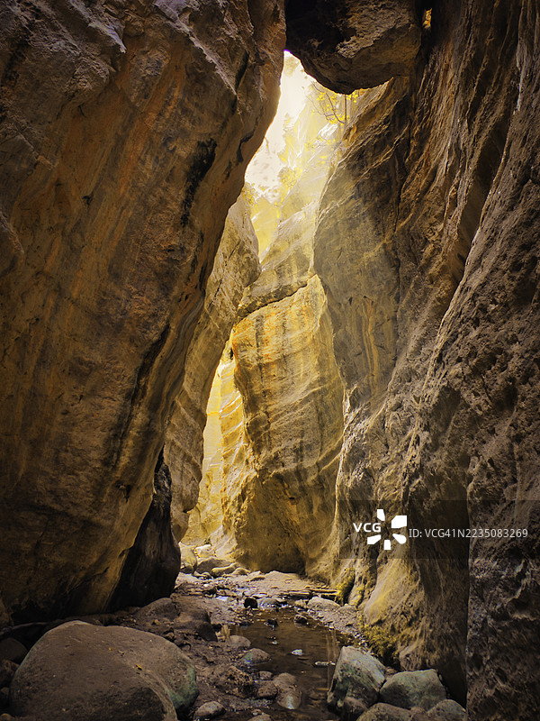 阳光洒进狭窄蜿蜒的峡谷，照亮了纹理分明的岩壁和下方的小溪，帕洛阿罗德斯，塞浦路斯图片素材
