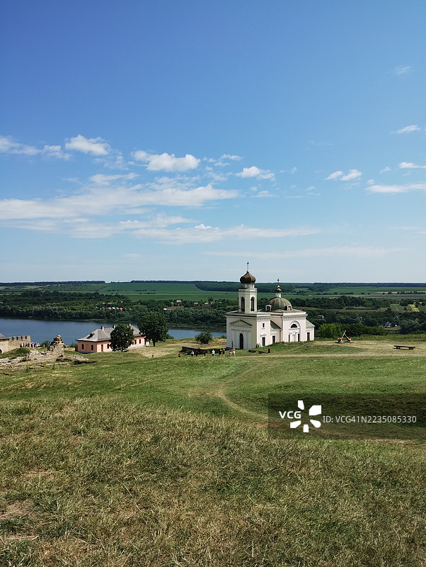乌克兰霍廷的山丘上，历史悠久的教堂俯瞰着河流和绿色的风景，蓝天映衬下的美丽景色。图片素材