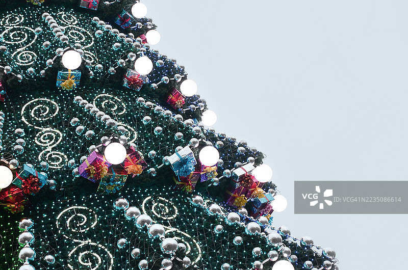 低角度视图下，装饰精美的圣诞树在晴朗的天空中，点缀着灯光和礼品盒。图片素材