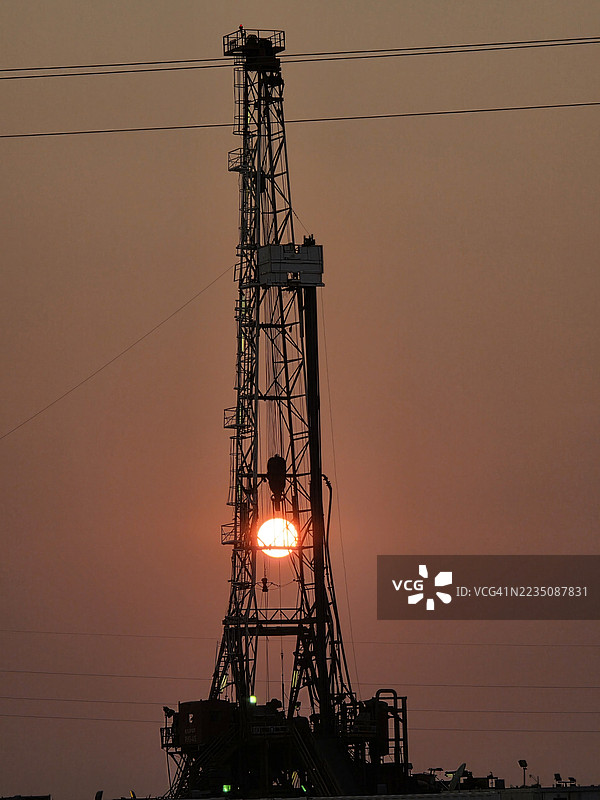 油井的剪影，夕阳完美地框在其结构内，象征着能源和工业。图片素材