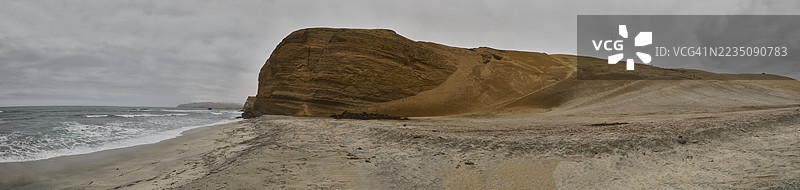 秘鲁帕拉卡斯崎岖海岸风景的全景，沙滩、海浪和一座巨大的岩石在多云的天空下。图片素材