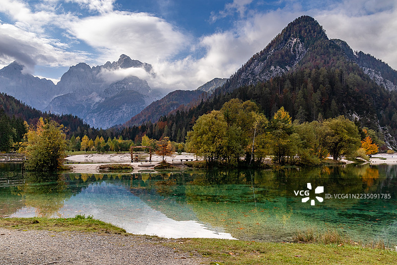 雄伟的山脉和色彩斑斓的秋季树木在阴云密布的天空下倒映在清澈的湖面上，斯洛文尼亚图片素材
