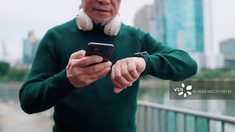 亚洲老年男子在公园锻炼前将智能手表连接到智能手机上图片素材