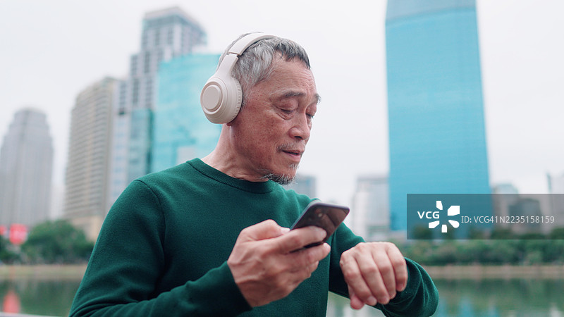 亚洲老年男子在公园锻炼前将智能手表连接到智能手机上图片素材